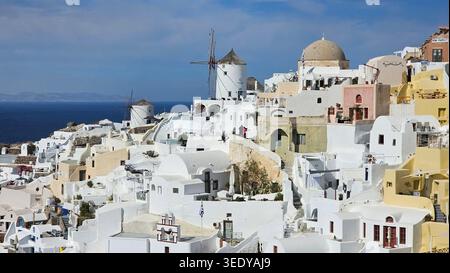Berühmte weiß getünchte Gebäude und traditionelle Windmühlen von Oia, Santorin stürzt die Klippe unter einem sonnigen Himmel, mit der tiefblauen Ägäis Stockfoto