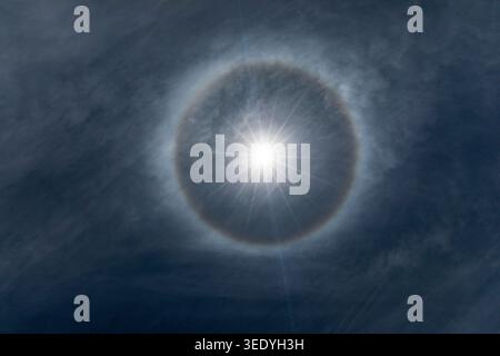 Perfekter 22-Grad-Eiskristall-Sonnenhalo leuchtet vor dunklen dramatischen Wolken über dem bolivianischen Altiplano, Südamerika Stockfoto