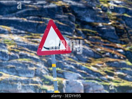 Rotes dreieckiges Warnschild für Hundeschlitten, montiert auf einem Metallpfosten vor rauer, flechtenbewachsener arktischer Felslandschaft in Grönland Stockfoto