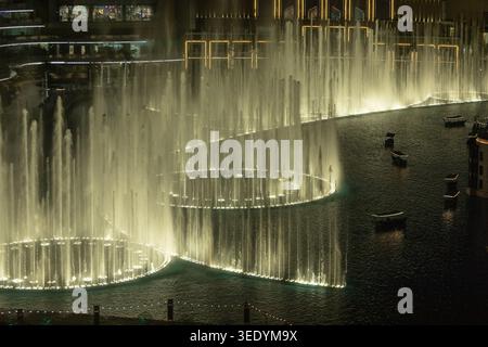 Wassershow der Dubai-Fontäne beleuchtet Fontänen in goldenem Licht bei Nacht auf dem Burj Lake mit traditionellen Abra-Booten, Downtown Dubai, Vereinigte Arabische Emirate Stockfoto