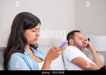 Teenager und Vater ignorieren sich gegenseitig, während sie auf ihren Mobiltelefonen surfen. Eine Szene digitaler Ablenkung und fehlender Kommunikation in den Lebenden Stockfoto