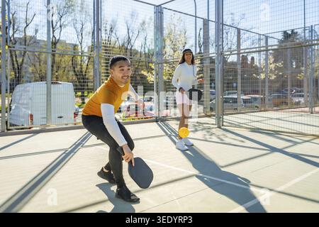 Junge, vielfältige Freunde genießen ein energisches Pickleball auf einem Outdoor-Court, halten Paddel und bleiben aktiv unter der hellen Sonne, Promo Stockfoto