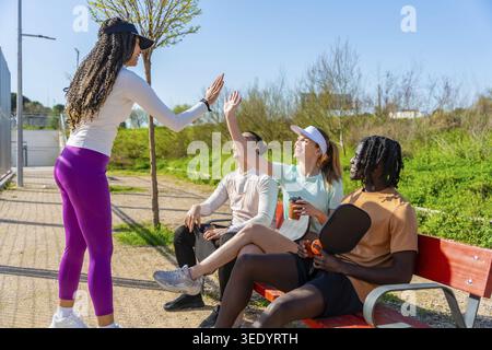 Verschiedene Gruppen von Freunden auf einem sonnigen Park Pickleball-Platz, halten inne, um mit einem hohen fünf geselligen, aktiven, lächelnden und Outdoor-Fit zu feiern Stockfoto