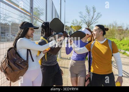 Verschiedene Gruppen fröhlicher junger Freunde, die Erfolg feiern, nachdem sie auf einem Platz im Freien Pickleball gespielt haben, Paddel und Bälle gehalten und das aktive Leben genossen haben Stockfoto