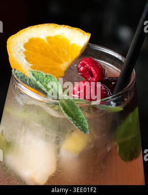 Erfrischendes Getränk mit Minze, Himbeeren und Orangenscheibe. Schwarzes Stroh sorgt für kräftigen Kontrast zu leuchtenden Farben. Glas gefüllt mit Eis und funkelndem liqui Stockfoto
