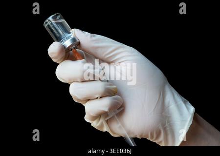 Nahaufnahme der Hände in weißen Handschuhen, die flüssiges Arzneimittel aus einer Durchstechflasche mit einer Spritze aufziehen. Stockfoto