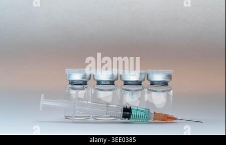 Medizinische Glasfläschchen des Impfstoffes und eine Spritze, die für die Injektion vorbereitet ist, auf grauem Hintergrund. Stockfoto