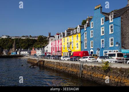 Blick auf die berühmten farbenfrohen Häuser entlang der Hafenfront mit geparkten Autos und einer Steinmauer am Meer in Tobermory, Schottland, Großbritannien. Stockfoto