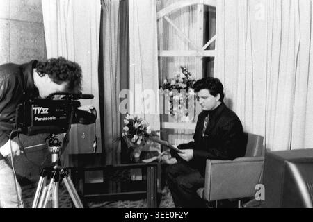 Sloviansk, 1997, Sloviansk Television. Dieses fesselnde Schwarzweiß-Archivfoto zeigt einen Kameramann, der eine große Panasonic-Videokamera verwendet, um einen männlichen Nachrichtenanker zu filmen, der aus einem Skript auf einem einfachen Studioset liest. Dieses authentische historische Dokumentarfilm bewahrt die einzigartige professionelle Atmosphäre der postsowjetischen Ära und zeigt regionale Nachrichtensendungen, Vintage-TV-Produktionsausrüstung, tägliche Medienabläufe und die äußerst wichtige historische Essenz eines friedlichen Donbas. Stockfoto