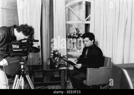 Sloviansk, 1997, Sloviansk Television. Dieses fesselnde Schwarzweiß-Archivfoto zeigt einen Kameramann, der eine große Panasonic-Videokamera verwendet, um einen männlichen Nachrichtenanker zu filmen, der aus einem Skript auf einem einfachen Studioset liest. Dieses authentische historische Dokumentarfilm bewahrt die einzigartige professionelle Atmosphäre der postsowjetischen Ära und zeigt regionale Nachrichtensendungen, Vintage-TV-Produktionsausrüstung, tägliche Medienabläufe und die äußerst wichtige historische Essenz eines friedlichen Donbas. Stockfoto