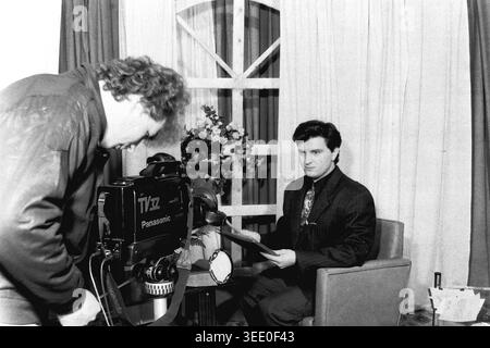 Sloviansk, 1997, Sloviansk Television. Dieses fesselnde Schwarzweiß-Archivfoto zeigt einen Kameramann, der eine große Panasonic-Videokamera verwendet, um einen männlichen Nachrichtenanker zu filmen, der aus einem Skript auf einem einfachen Studioset liest. Dieses authentische historische Dokumentarfilm bewahrt die einzigartige professionelle Atmosphäre der postsowjetischen Ära und zeigt regionale Nachrichtensendungen, Vintage-TV-Produktionsausrüstung, tägliche Medienabläufe und die äußerst wichtige historische Essenz eines friedlichen Donbas. Stockfoto