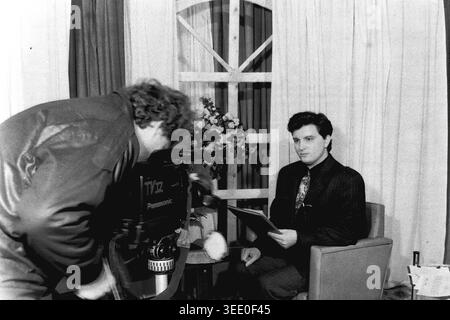 Sloviansk, 1997, Sloviansk Television. Dieses fesselnde Schwarzweiß-Archivfoto zeigt einen Kameramann, der eine große Panasonic-Videokamera verwendet, um einen männlichen Nachrichtenanker zu filmen, der aus einem Skript auf einem einfachen Studioset liest. Dieses authentische historische Dokumentarfilm bewahrt die einzigartige professionelle Atmosphäre der postsowjetischen Ära und zeigt regionale Nachrichtensendungen, Vintage-TV-Produktionsausrüstung, tägliche Medienabläufe und die äußerst wichtige historische Essenz eines friedlichen Donbas. Stockfoto