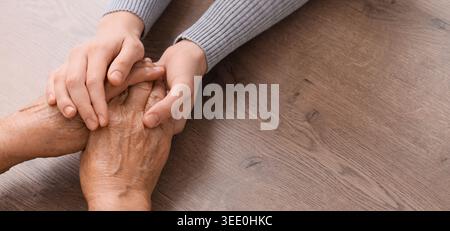 Junge Frau, die Großmutters Hände auf hölzernem Hintergrund hält, mit Platz für Text. Konzept der Pflege und Betreuung Stockfoto