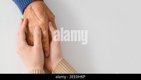 Frau, die Großmutters Hand auf hellem Hintergrund hält, mit Platz für Text, Ansicht von oben. Konzept der Pflege und Betreuung Stockfoto