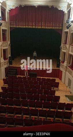 Cremona, Italien 9. April 2026 Schauspieler, die auf einer Theaterbühne mit einem großen roten Vorhang und zahlreichen leeren Plätzen im eleganten Auditorium vor Stockfoto