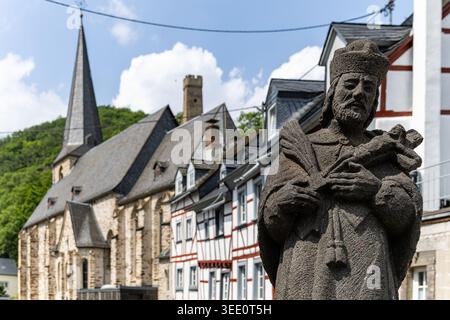 Blick auf die Steinstatue des Heiligen Johannes von Nepomuk mit der historischen Dreifaltigkeitskirche und traditionellen Fachwerkhäusern unter blauem Himmel Stockfoto