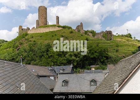 Blick auf die historische Burgruine Monreal auf einem üppig grünen Hügel über traditionellen Schieferdächern unter bewölktem Himmel in Monreal, Rheinland-Pfalz Stockfoto