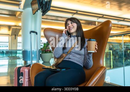 Eine Reisende Frau, die Kaffee trinkt und am Flughafen telefoniert Stockfoto
