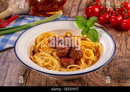 Appetitliche Spaghetti mit herzhaften Fleischbällchen mit frischem Basilikum, präsentiert in einer weißen Schüssel auf rustikalem Holztisch Stockfoto