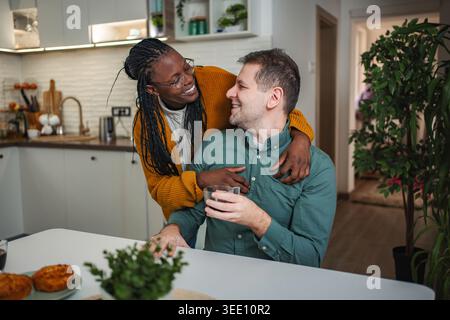 Glückliches multirassisches Paar, das sich in der Küche umschließt Stockfoto