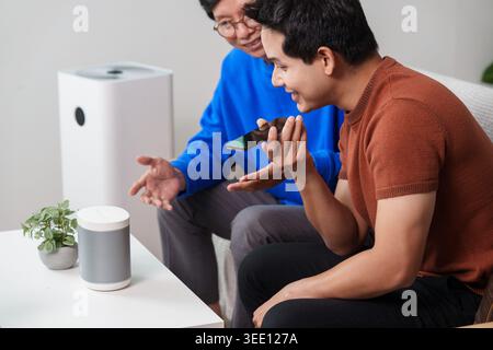 Asiatischer Senior und junger Mann mit intelligentem Home-Sprachassistenten zu Hause Stockfoto