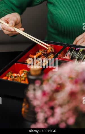 Das Mädchen isst Essen in Soße aus der bento-Box mit Essstäbchen. Blinken Stockfoto