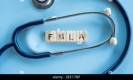 Medizinisches Stethoskop, das hölzerne Buchstaben-Fliesen umrahmt, die FMLA Akronym für Familie und medizinisches Leave Act auf blauer Oberfläche buchstabieren Stockfoto