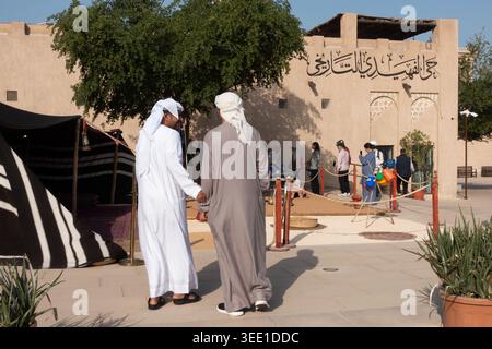Zwei arabische Männer beobachten eine Gruppe chinesischer Touristen im historischen Viertel Al Fahidi in Old Dubai, Dubai, VAE. Stockfoto