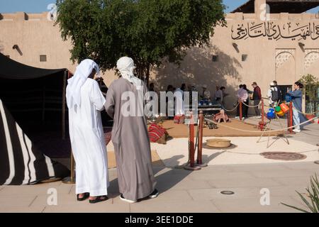 Zwei arabische Männer beobachten eine Gruppe chinesischer Touristen im historischen Viertel Al Fahidi in Old Dubai, Dubai, VAE. Stockfoto