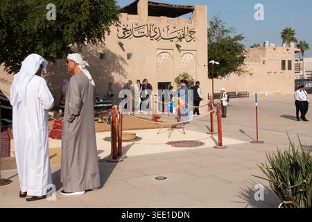 Zwei arabische Männer beobachten eine Gruppe chinesischer Touristen im historischen Viertel Al Fahidi in Old Dubai, Dubai, VAE. Stockfoto