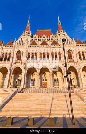 Ein paar Spaziergänge in der Nähe des Parlamentsgebäudes in Budapest. Die Sonne untergeht hinter dem historischen Gebäude und wirft lange Schatten auf die Stufen. Stockfoto