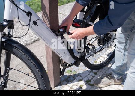 Junger Mann mit Helm, der sein Elektrofahrrad mit einem Schloss an einem Fahrradständer in der Nähe des Wassers sichert Stockfoto