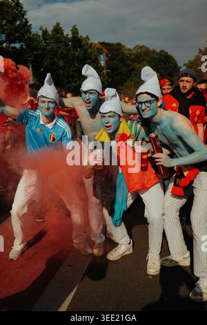 Belgische Fans posieren als Schlümpfe in blauer Gesichtsfarbe und weißen Hüten unter rotem Rauch während des fanmarsches in Köln vor der UE Stockfoto
