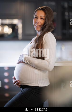 Schwangere Frau lächelt warm, während sie in ihrer Küche steht Stockfoto