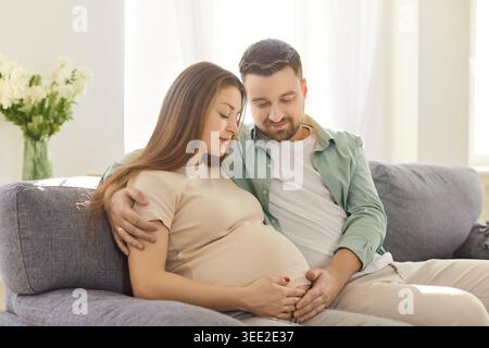 Liebevoll erwarten, dass ein Paar zu Hause kuschelt, Hände auf dem schwangeren Bauch, ein ruhiger Moment Stockfoto