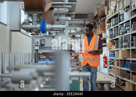 Der afroamerikanische Mann betreibt Maschinen und inspiziert Produktionswerkzeuge mit einem digitalen Tablet in einer Fabrik. Stockfoto