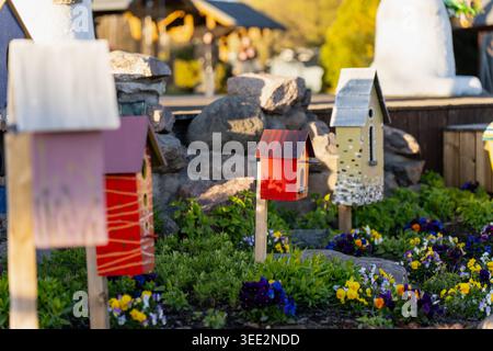 Bunte Vogelnistkästen in einem öffentlichen Blumenbeet in der Nähe einer Steinmauer, die sich auf Gartendesign, Umweltschutz und Kunsthandwerk konzentriert Stockfoto