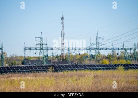 Industrieller Solarpark integriert mit Hochspannungs-Strommasten und einem Telekommunikationsturm in einer ländlichen Landschaft, die moderne Energie und Energie repräsentiert Stockfoto