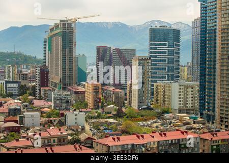 Panoramablick auf eine sich entwickelnde Stadt mit moderner Architektur und im Bau befindlichen Wolkenkratzern vor dem Hintergrund des majestätischen, schneebedeckten Kaukasus. Stockfoto