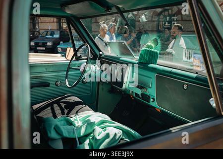 BERLIN, DEUTSCHLAND - 2. MAI 2026. Türkisfarbener Innenraum eines Oldtimer mit Lenkrad, Armaturenbrett und Reflexionen der Besucher des Oldtimer Open Air Stockfoto
