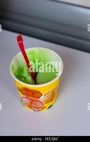 Grüner Pistazien-Eislöffel im Becher mit Rotem Löffel Stockfoto