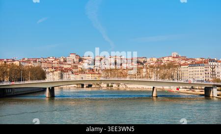 Lyon, Frankreich - 19. März 2026: Moderne Fußgängerbrücke über die Saone mit Blick auf historische Gebäude am Hang unter klarem blauem Himmel Stockfoto
