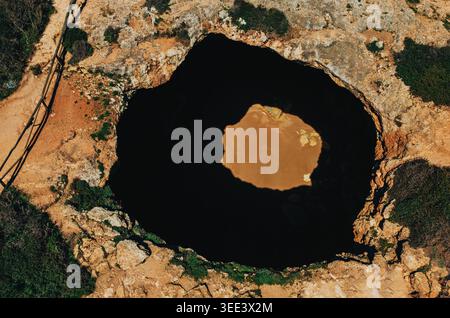 Blick aus der Vogelperspektive auf die massive Küstenhöhle mit verstecktem Sandstrand, umgeben von zerklüftetem felsigem Gelände und dramatischen Schatten. Portugal. Benagil Stockfoto