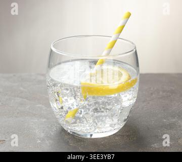 Erfrischendes Wasser mit Zitrone im Glas auf grauem, strukturiertem Tisch, Nahaufnahme Stockfoto