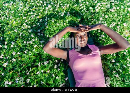 Frau mit Blick aus dem Hochwinkel, die in einem weißen Blumenfeld liegt und die Augen vor der Natur des Sonnenfrühlingsparks schützt Stockfoto
