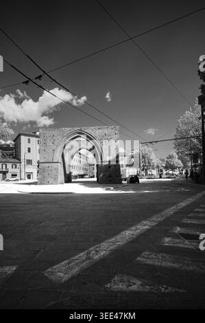 Schwarzweißfoto mit der Porta Saragozza in Bologna, Italien. Der alte Backsteinbogen umrahmt eine belebte Straße mit Gebäuden, Autos und mehr Stockfoto