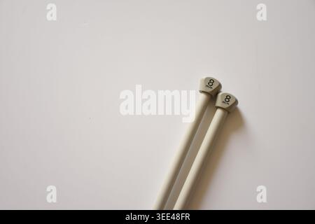 Graue Stricknadeln auf einem sauberen weißen Tisch mit minimalistischer Zusammensetzung und sanfter natürlicher Beleuchtung. Perfekt für Strickkonzepte, Stockfoto