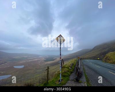 Straßenschild mit einem Aufkleber am Conor Pass Gipfel mit einem atemberaubenden Blick über das Tal der Dingle Peninsula und die Seen in Kerry, Irland Stockfoto