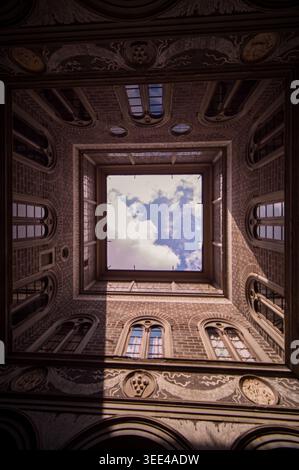Aus einem historischen Innenhof in Florenz, Italien, aus der Perspektive nach oben geschossen und der Himmel und die weißen Wolken durch eine quadratische Öffnung enthüllt werden. Das umgebende Wal Stockfoto
