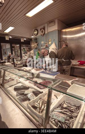 Zwei erfahrene Fischhändler bereiten aktiv frischen Fisch hinter einer gut sortierten Verkaufstheke an einem belebten Marktstand in Florenz, Italien, zu. Die Stockfoto